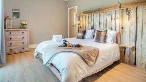 Une chambre à coucher avec une tête de lit en bois, un lit avec du linge de maison blanc, une commode et une table de chevet sur laquelle se trouvent une bouilloire et une théière.