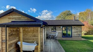 Une cabane en bois avec une salle de bain, une terrasse avec une table et des chaises, et un bâtiment séparé doté d’une porte coulissante.