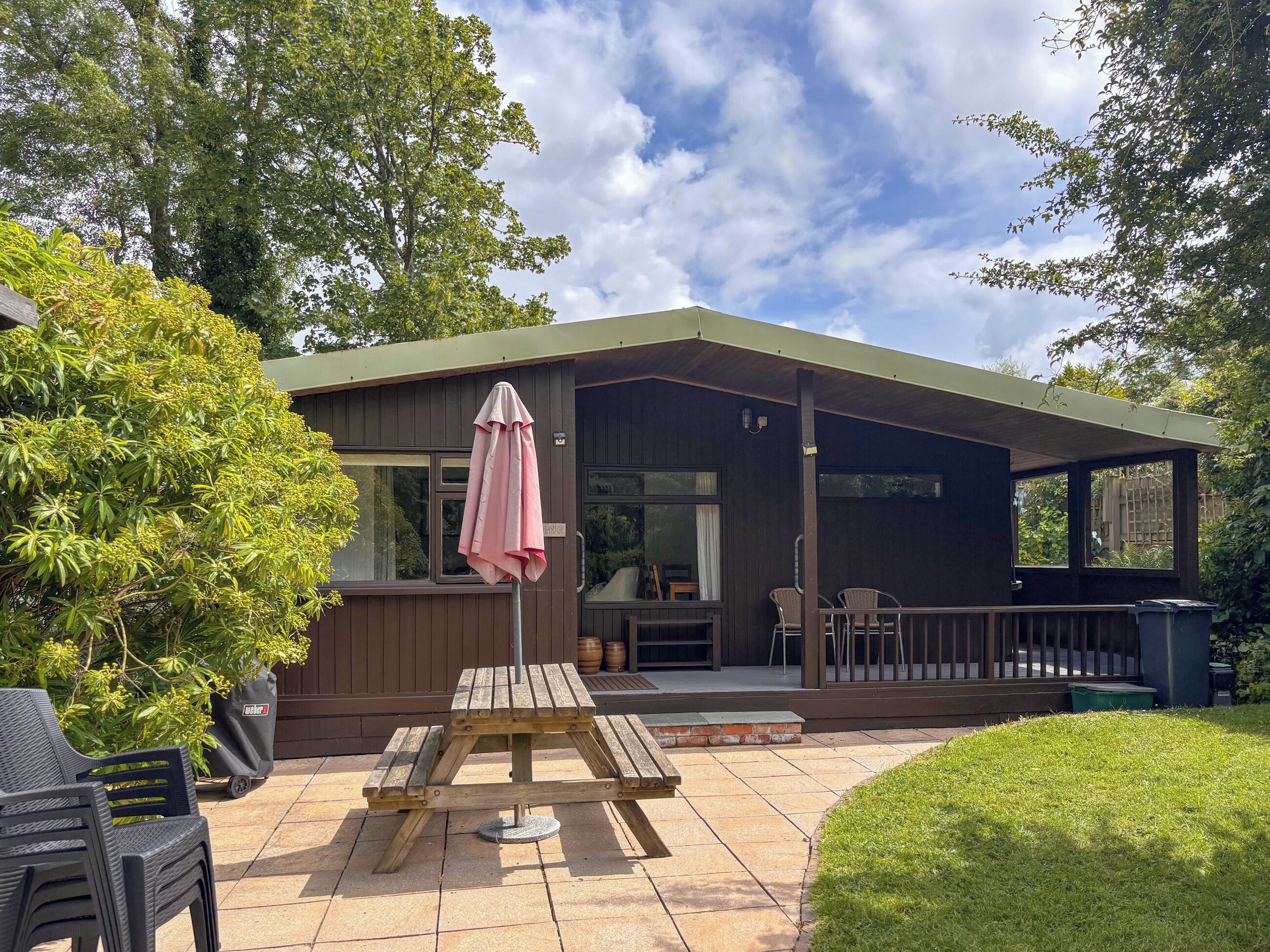 Eine Holzterrasse mit Picknicktisch und -stühlen, ein überdachter Patio-Bereich und Blick ins grüne Umland.