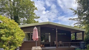 Een houten terras met een picknicktafel en stoelen, een overdekte patio en uitzicht op de omliggende begroeiing.