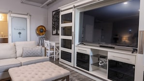 Un salon moderne avec un canapé, un pouf et un téléviseur posé sur un meuble.