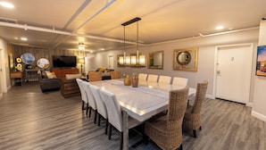 Un espace repas moderne avec une grande table, des chaises en osier et un téléviseur en arrière-plan.