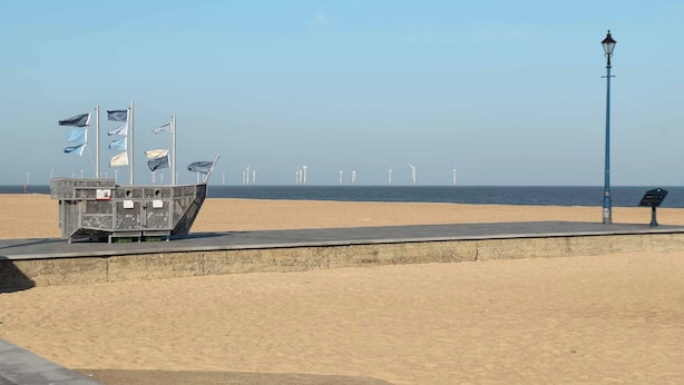 Une plage avec une barrière en béton, des drapeaux et un lampadaire.