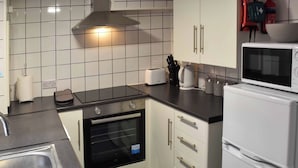 Une cuisine compacte équipée d’un four encastré, d’un four à micro-ondes et d’un évier. On y trouve des placards avec des poignées et un plan de travail sur lequel sont disposés divers objets.