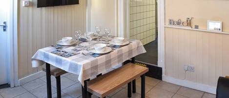 A dining area with a table set for four, a bench, a TV mounted on the wall, and a tiled backsplash.