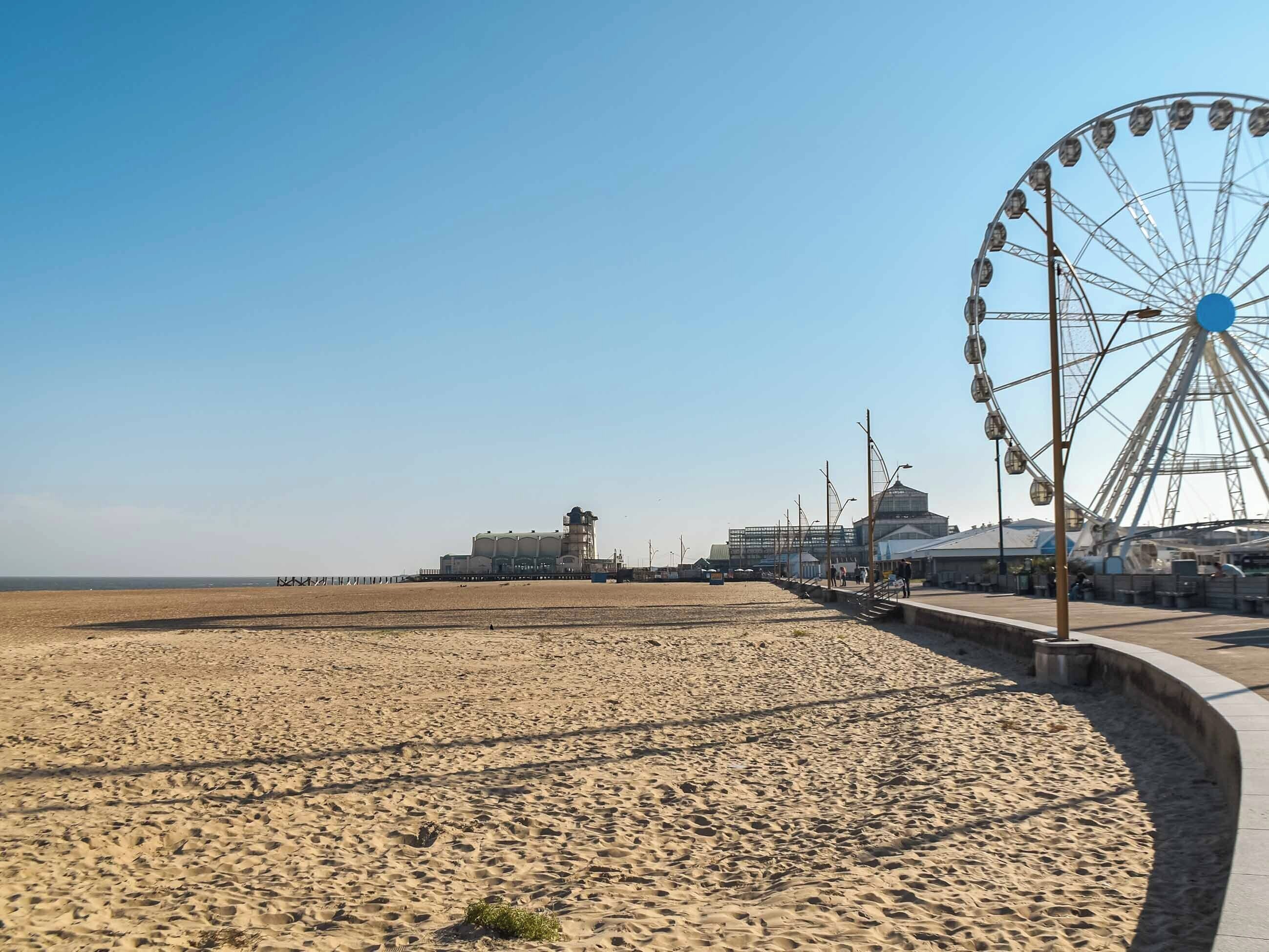 Uma praia arenosa com uma roda gigante e um prédio grande ao fundo.
