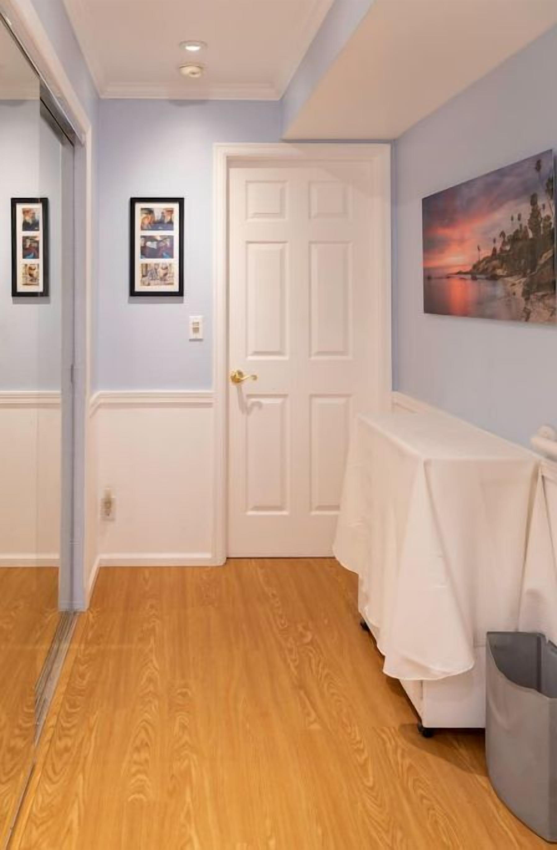 A hallway with wooden flooring, a white door, and a table with a white tablecloth.