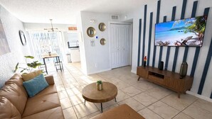 Een woonkamer met een leren bank, een ronde salontafel, een televisie aan de muur en een deur die naar een andere kamer leidt.