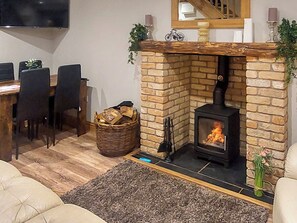 Een gezellige woonkamer met een stenen open haard, een eethoek met stoelen en een aan de muur bevestigde televisie.