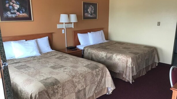 Una habitación de hotel con dos camas, una mesita de noche, una lámpara y dos cuadros en la pared.