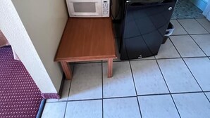 Una kitchenette pequeña con microondas, cafetera y refrigerador compacto.