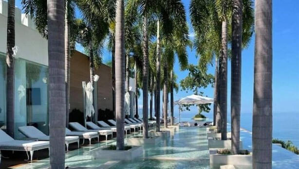 Un espace piscine avec des chaises longues, des palmiers et une vue sur l’océan.