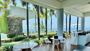 Un espace de restauration extérieur moderne avec vue sur l’océan, comprenant une table ronde avec des chaises, un coin bar et un mur en pierre en arrière-plan.