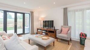 A living room with a sofa, armchair, ottoman, TV, and a wooden side table with books and glasses. - 3 bedroom accommodation in Beauworth, near Alresford (Beauworth, near Alresford)