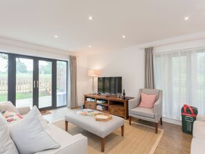 A living room with a sofa, armchair, ottoman, TV, and a wooden side table with books and glasses. - 3 bedroom accommodation in Beauworth, near Alresford (Beauworth, near Alresford)
