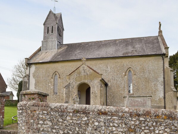 A church with a stone wall in front, a bell tower, and a simple arched entrance.