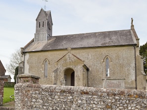 En kirke med en stenvæg foran, et klokketårn og en enkel buegang.