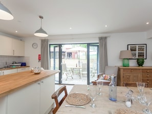 A kitchen with a wooden countertop, a dining table with chairs, a green lamp, and a framed picture on the wall.