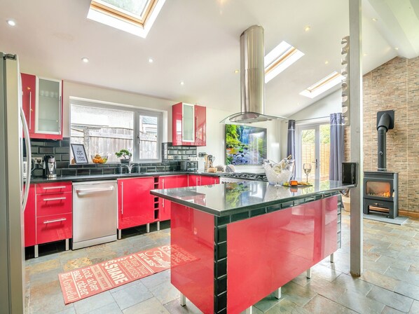 A modern kitchen with red cabinetry, a central island, a built-in stove, and a large window overlooking a garden.