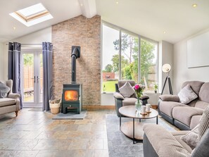 A cozy living room with a stone fireplace, comfortable seating, and large windows offering a view of the outdoors.