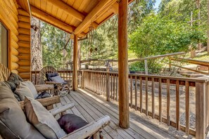 A wooden deck with a railing, a log cabin structure, and a view of the surrounding forest.