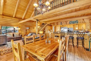 A log cabin interior with a dining area, kitchen, and a staircase leading to an upper level.