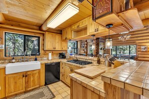 A wooden cabin kitchen with a large island, built-in cabinets, and a view of the forest.