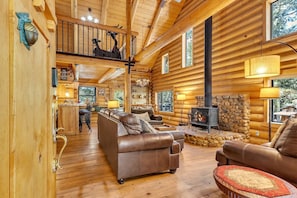 A log cabin interior with a fireplace, leather sofas, a dining area, and a balcony. - "Rustic Elegance - A Woodland Escape" (Idyllwild-Pine Cove)