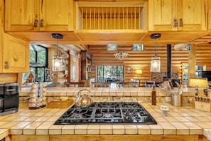 Interior de una cabaña de madera con cocina que incluye estufa a gas, armarios de madera y comedor con mesa y sillas.