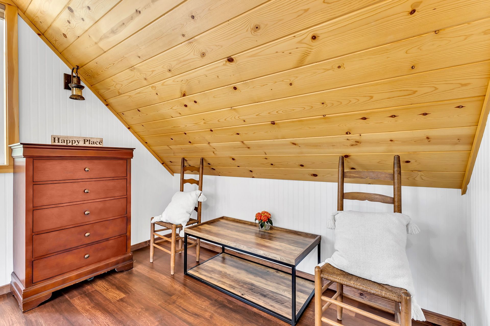 A room with a wooden ceiling, a wooden dresser, a table with chairs, and a sign that reads 'Happy Place'.