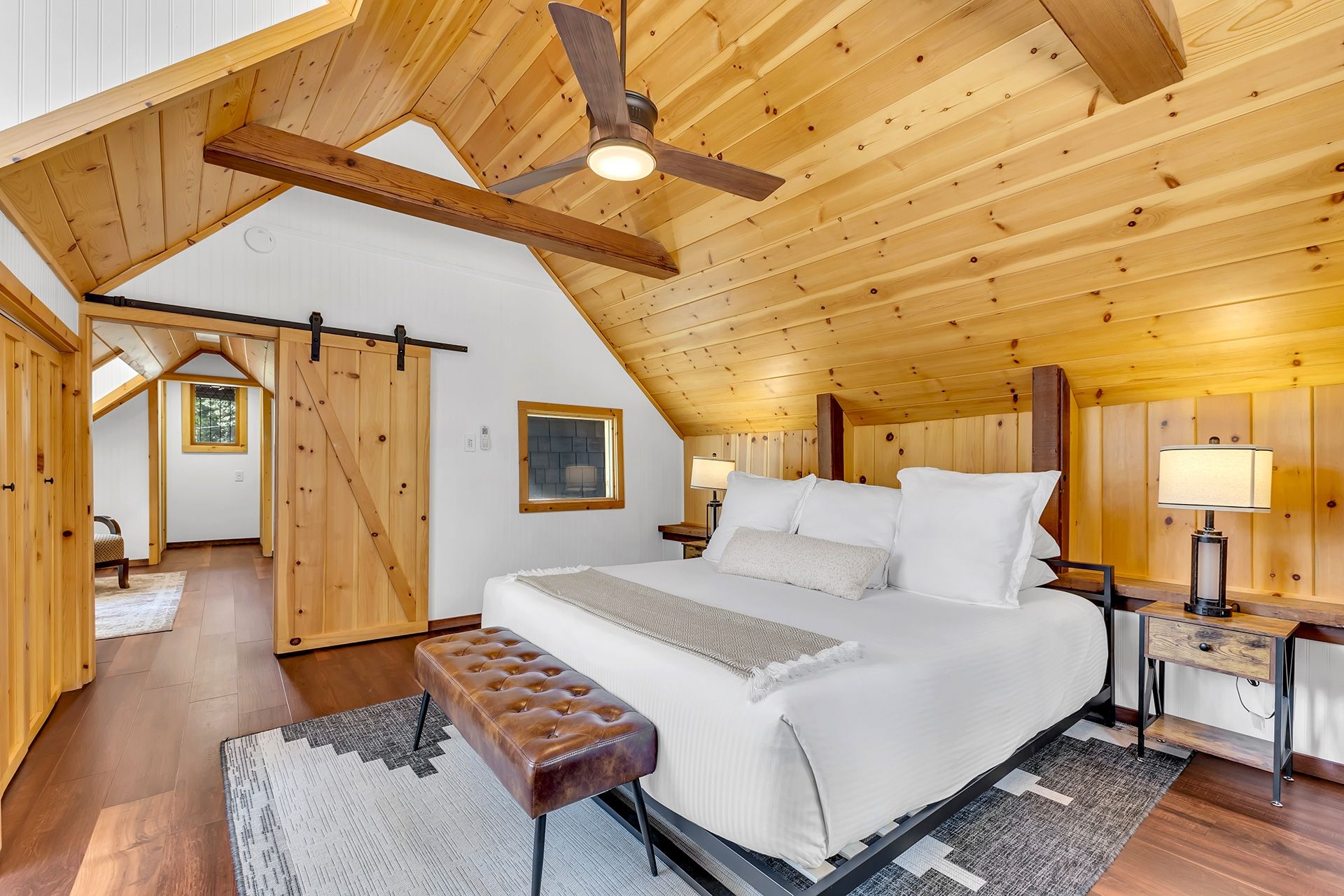 Een slaapkamer met een groot bed, een plafondventilator, houten wanden en uitzicht op een gang.