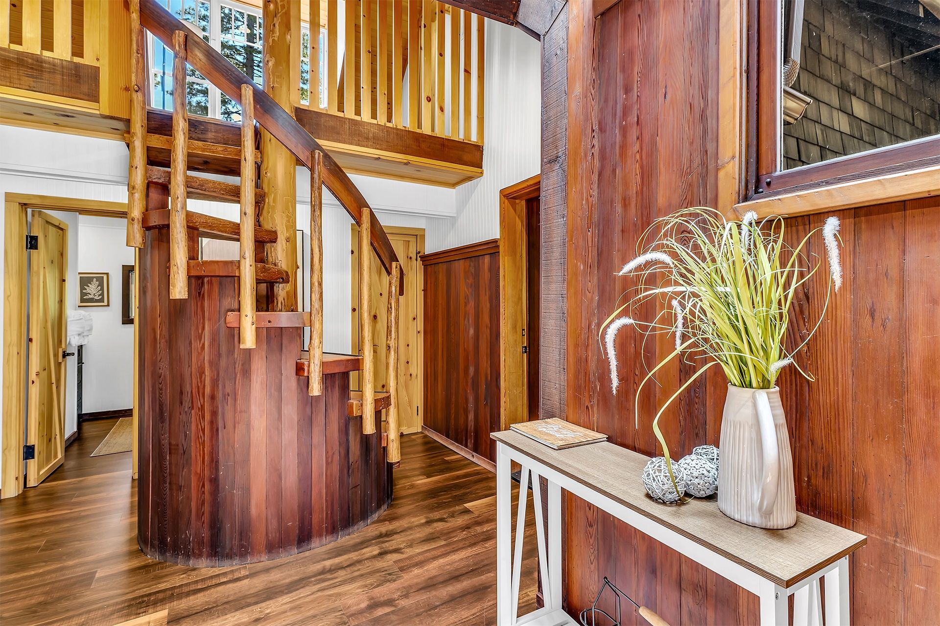 Eine Holztreppe führt zu einer oberen Ebene, ein weißer Konsolentisch mit Dekorationen und eine Holzwand mit einem Fenster.