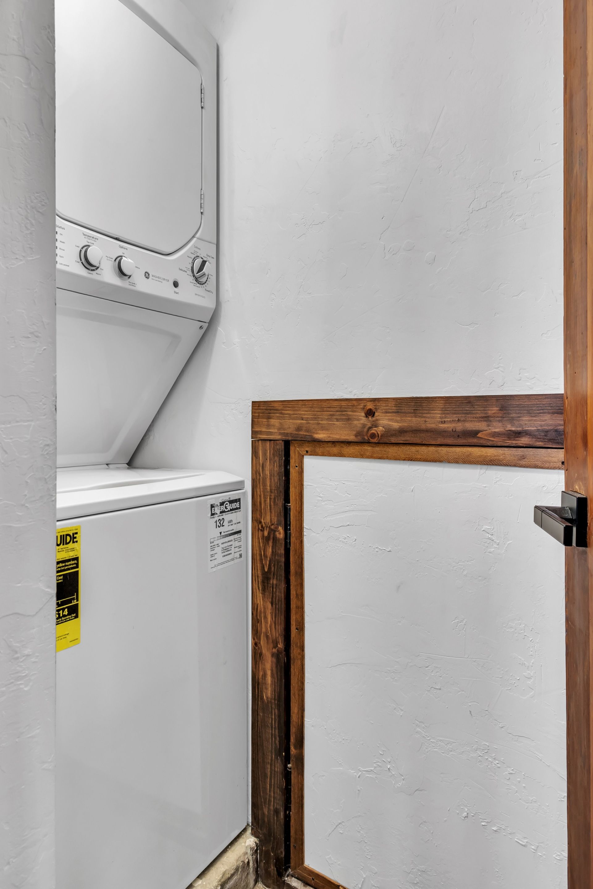 Une buanderie équipée d’un lave-linge et d’un sèche-linge, avec un cadre de porte en bois et un mur blanc à texture.