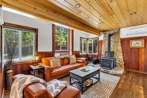 A cozy living room with a stone fireplace, leather furniture, and large windows. - Hobbit House - Cozy Fireplace Retreat In Town (Idyllwild-Pine Cove)