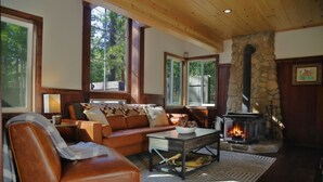 Ein gemütliches Wohnzimmer mit Kamin aus Stein, Ledersofa und großen Fenstern.
