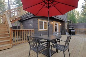 Una terraza con una mesa y sillas, un paraguas rojo y una escalera de madera.