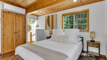 Une chambre à coucher avec un grand lit, un plafond en bois, une fenêtre donnant sur la forêt et une armoire en bois.