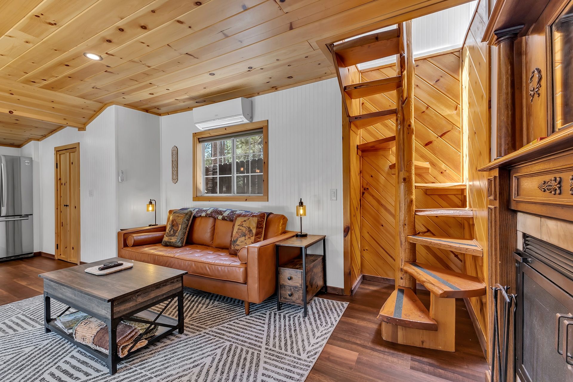 Un salon chaleureux avec un plafond en bois, un canapé en cuir, une table basse et une cheminée agrémentée d’un escalier en bois.