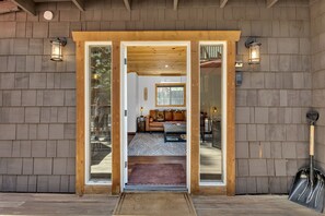 A wooden exterior with a glass door entrance, a brown bench outside, and a shovel to the right. - La Petite - cozy fireplace cabin in town (Idyllwild-Pine Cove)