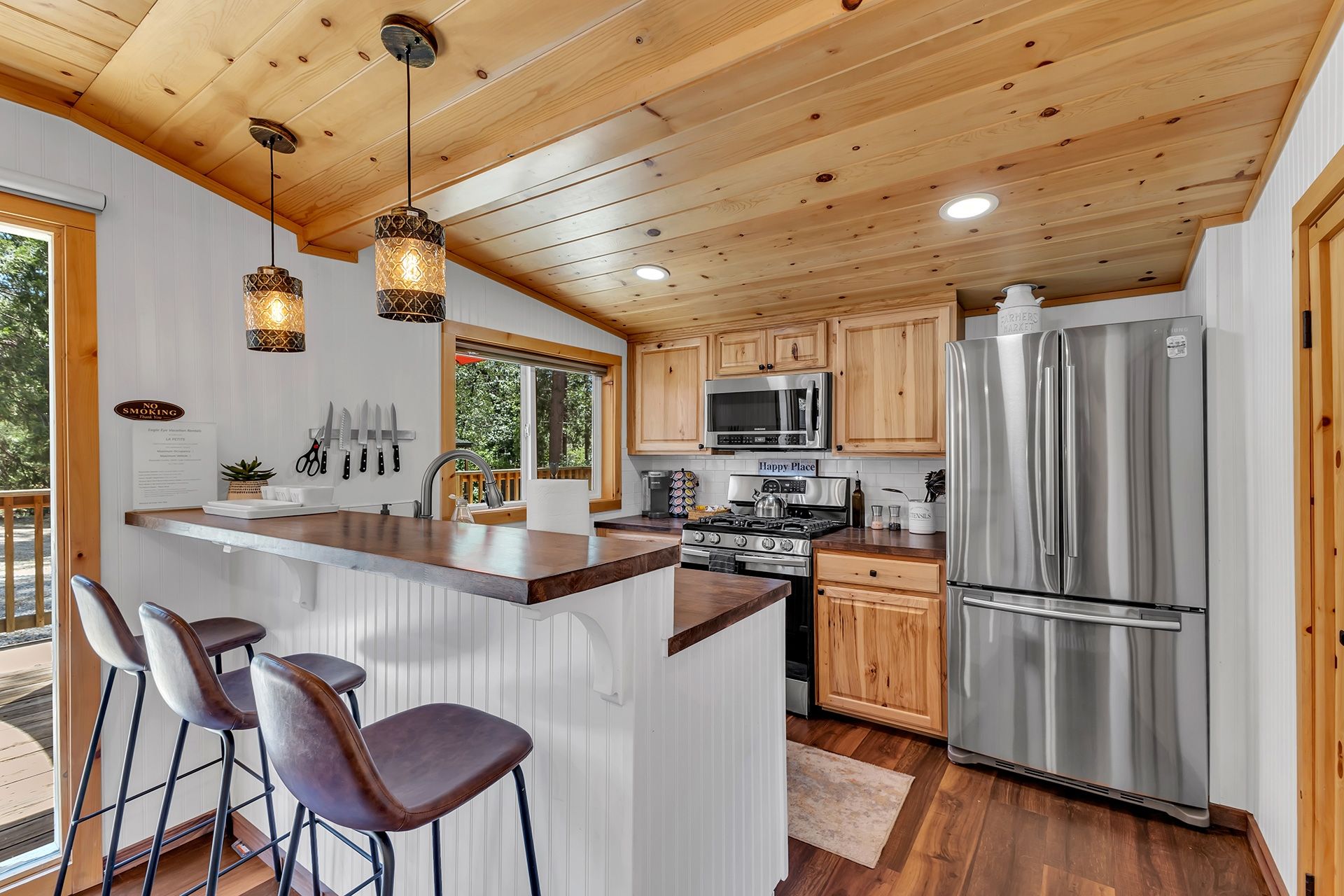 A modern kitchen with wooden cabinets, stainless steel appliances, and a bar area with stools.