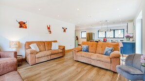 A modern living room with two sofas, a coffee table, and a dining area with a kitchen in the background. - This stunning property certainly has the wow factor. (Finghall, Leyburn)
