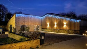 A modern building with a wooden facade, a stone wall, and a landscaped garden area. - This stunning property certainly has the wow factor. (Finghall, Leyburn)