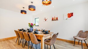 A dining area with a wooden table set for six, surrounded by six chairs, with pendant lights above. - This stunning property certainly has the wow factor. (Finghall, Leyburn)