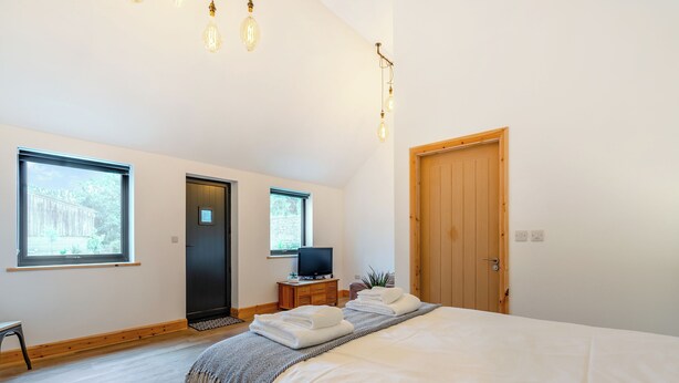 A bedroom with a large bed, a television on a wooden side table, and two windows. - This stunning property certainly has the wow factor. (Finghall, Leyburn)