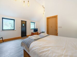 A bedroom with a large bed, a television on a wooden side table, and two windows. - This stunning property certainly has the wow factor. (Finghall, Leyburn)