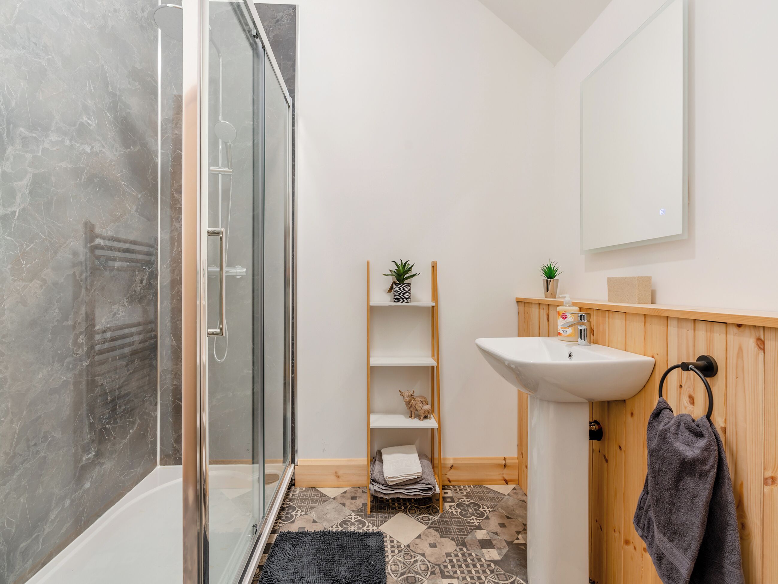 Une salle de bain dotée d’une douche à parois de verre, d’un lavabo avec un meuble-vasque en bois, d’un miroir et d’une étagère contenant des articles de toilette.
