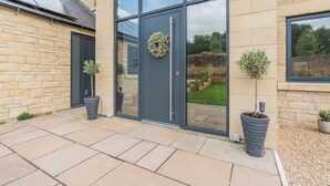 A modern building with a stone facade, large glass windows, and a door with a wreath. There are potted plants on the ground. - This stunning property certainly has the wow factor. (Finghall, Leyburn)