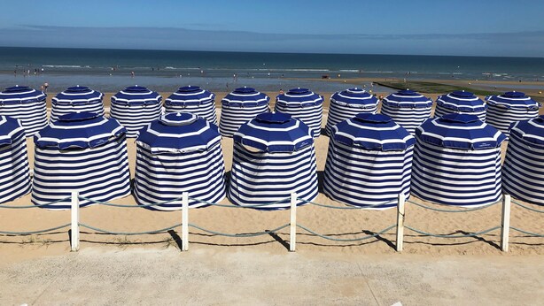 A beach with rows of striped beach umbrellas and a clear view of the ocean.