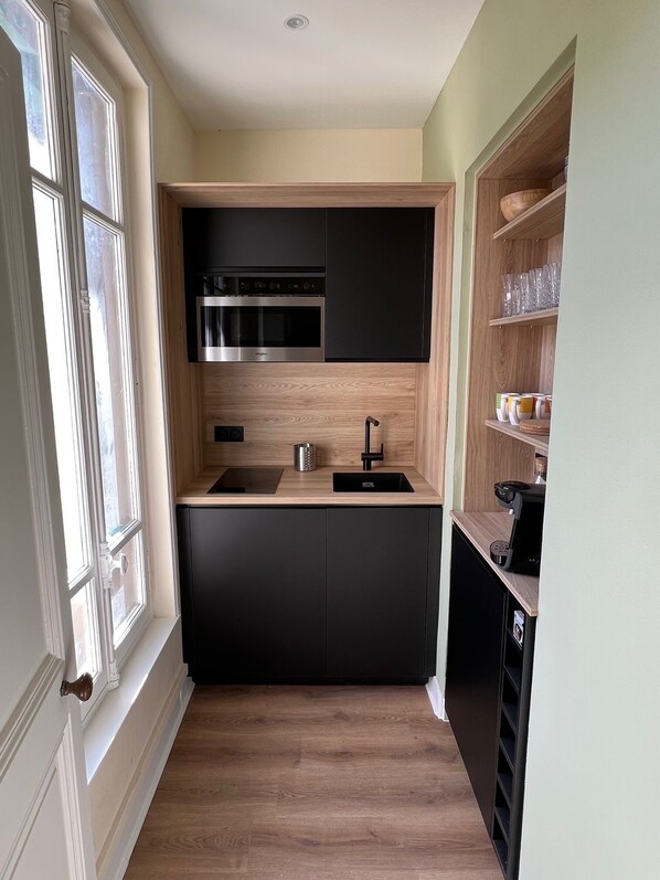 A compact kitchen with black cabinets, a stainless steel microwave, and a coffee machine.