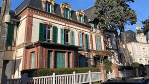 A two-story building with a brick facade, green shutters, and a white picket fence.